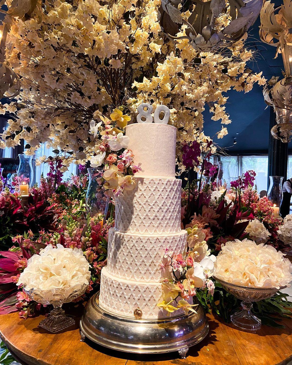 Bolo de quatro andares com o número 80 cercado de flores