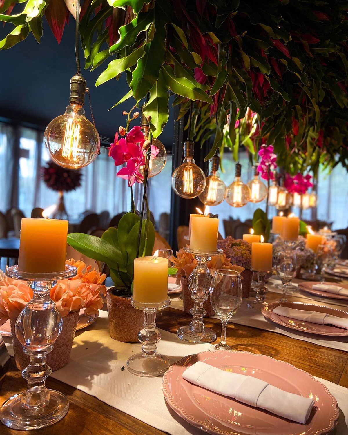 Mesa comprida com pratos rosa, velas e orquídeas